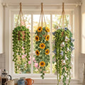 Three crochet hanging plants - string of pearls, sunflower and lily of the valley - in a kitchen window