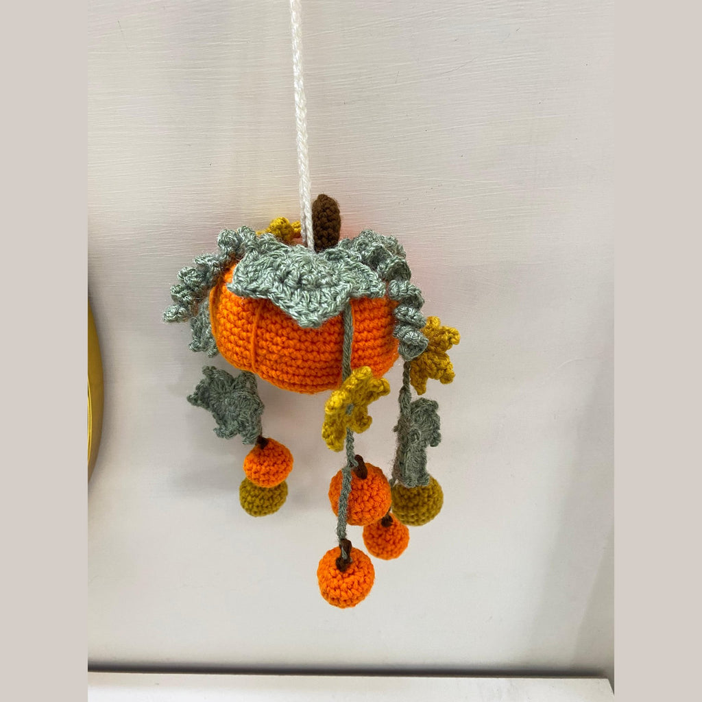 Orange crochet pumpkin wall hanging with a leafy collar and dangling mini pumpkins