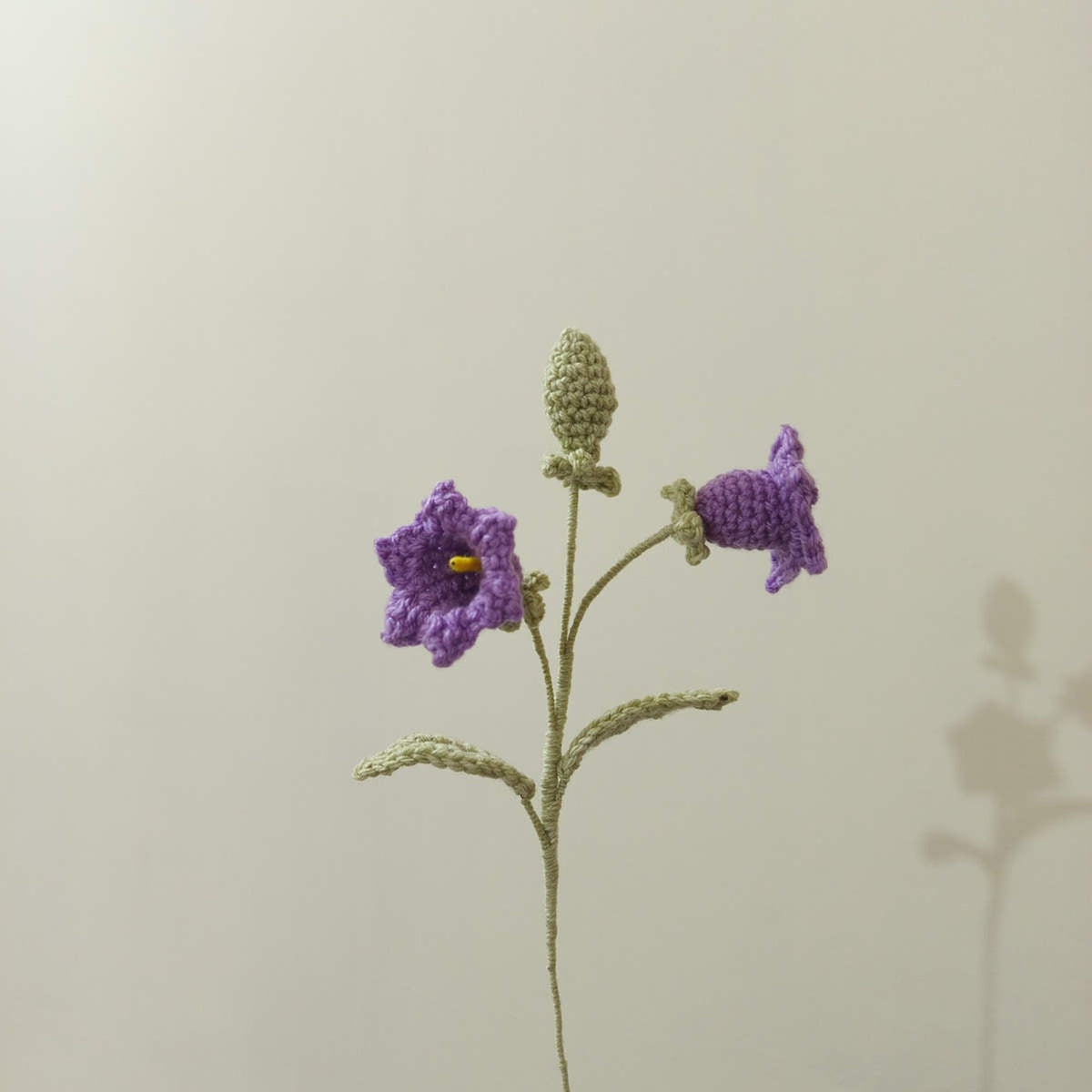 Crochet lily of the valley flower stem with deep purple bell flowers and green leaves