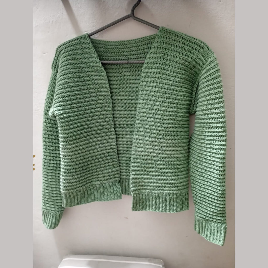 Open-front green crochet ribbed cardigan hanging against a white wall