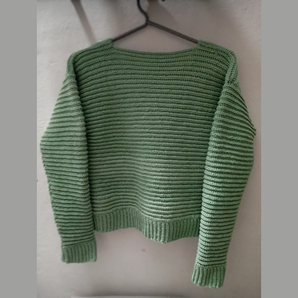 Back view of the green crochet rib stitch cardigan on a hanger