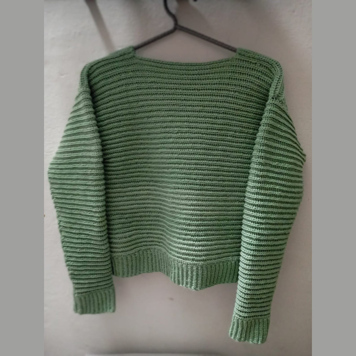 Back view of the green crochet rib stitch cardigan on a hanger