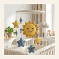 Crochet nursery mobile with a smiling sun, clouds and stars above a cot