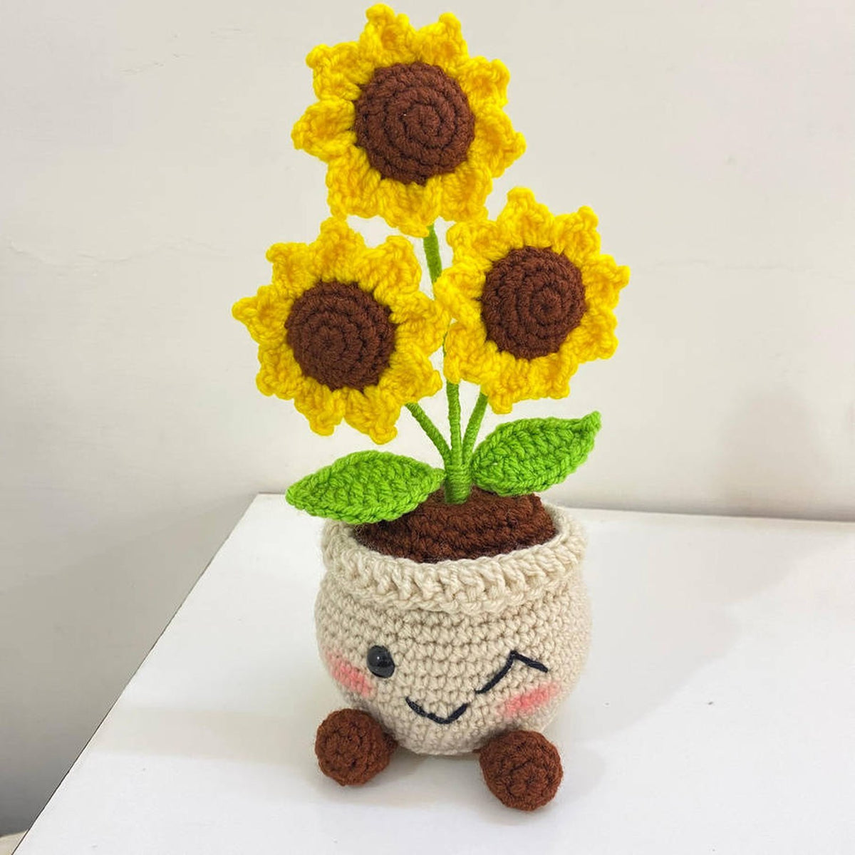 Crochet sunflower plant pot with a smiling face and three yellow sunflowers